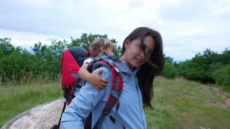 Photo for Mother hiking with child carrying son in backpack carrier outside during trekking - Royalty Free Image