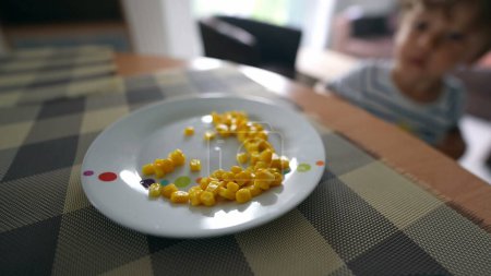 Téléchargez les photos : Un enfant attrape du maïs dans une assiette Un petit garçon attrape de la nourriture - en image libre de droit