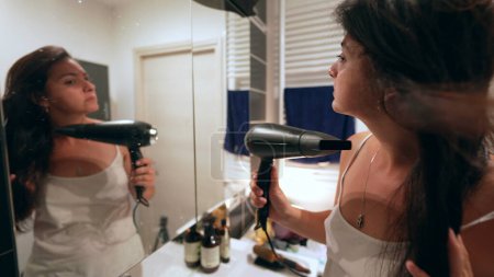 Téléchargez les photos : Femme sèche les cheveux devant le miroir de salle de bain - en image libre de droit