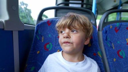 Téléchargez les photos : Un enfant réfléchi équitation bus passager enfant sur le siège de transport public regardant par la fenêtre - en image libre de droit