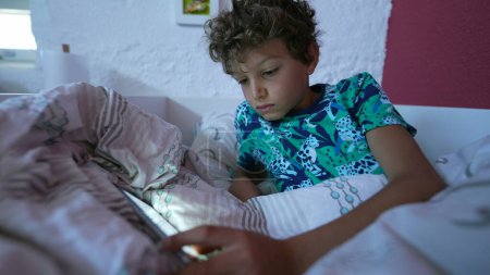 Téléchargez les photos : Navigation enfant internet en ligne couché dans le lit le matin en regardant l'écran - en image libre de droit