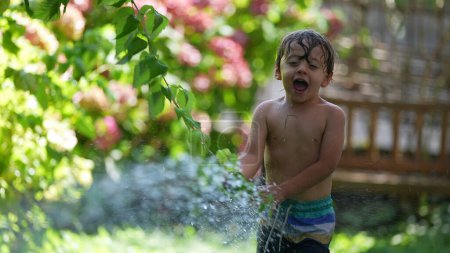 Téléchargez les photos : Enfant jouant dehors avec vaporisateur d'eau riant et souriant - en image libre de droit