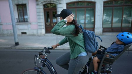 Foto de Bicicleta madre en calle urbana con niño en asiento trasero durmiendo - Imagen libre de derechos
