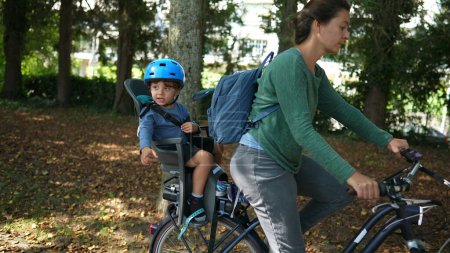 Téléchargez les photos : Enfant assis sur une chaise arrière de vélo avec sa mère à vélo - en image libre de droit