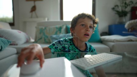 Téléchargez les photos : Fatigué petit garçon bâillement navigation Internet en ligne à l'aide de la souris et le clavier - en image libre de droit