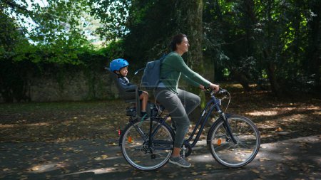Téléchargez les photos : Mère à vélo à l'extérieur au parc avec enfant sur le siège arrière - en image libre de droit