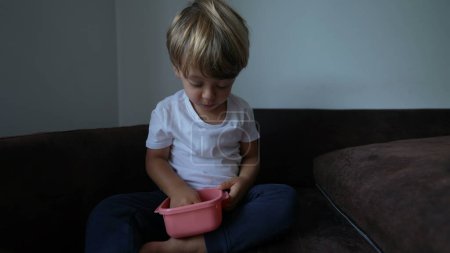 Téléchargez les photos : Petit garçon grignoter de la nourriture assis sur le canapé - en image libre de droit