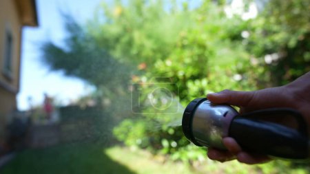 Foto de Manguera de agua de mano que riega el jardín durante el día soleado - Imagen libre de derechos