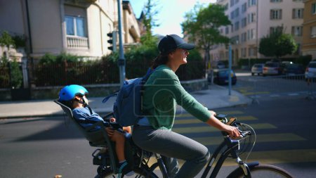 Photo for Woman riding bicycle in urban street with child in back seat - Royalty Free Image