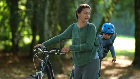 Téléchargez les photos : Bonne mère et enfant à l'extérieur portant vélo bambin dans le siège arrière de vélo - en image libre de droit
