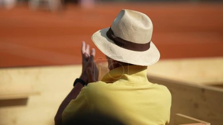 Photo for Spectator watching tennis match game clapping hands cheering from stadium seat wearing panama hat - Royalty Free Image