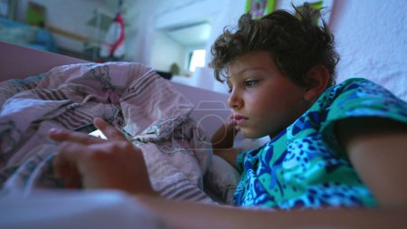 Téléchargez les photos : Enfant regardant du contenu en ligne sur un smartphone au lit - en image libre de droit