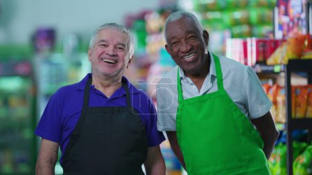Foto de Felices y diversos trabajadores senior de pie en la tienda de comestibles sonriendo a la cámara con uniformes. Trabajadores mayores del personal brasileño - Imagen libre de derechos
