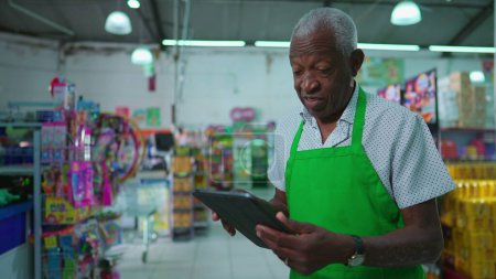 Photo for African American senior employee of supermarket using tablet device standing inside grocery store, job occupation of a black older person at workplace, checking inventory - Royalty Free Image