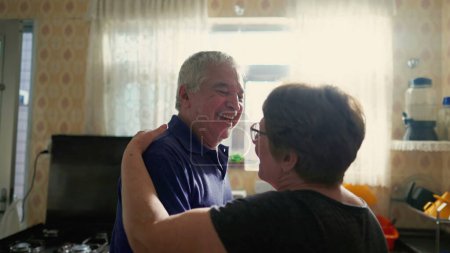 Photo for Elderly Couple Dancing in Morning Light by Kitchen Window, Senior Husband and Wife in Loving Embrace - Royalty Free Image