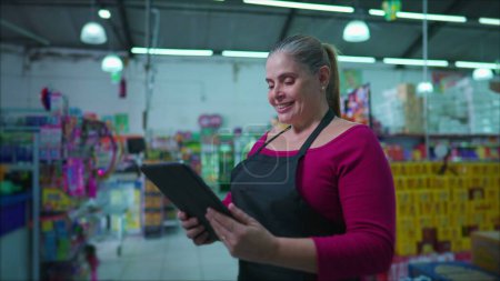 Téléchargez les photos : Femme entrepreneur propriétaire de la chaîne de supermarchés tenant tablette appareil changeant l'émotion de neutre à heureux debout à l'intérieur des affaires. Femme d'âge moyen utilisant la technologie moderne - en image libre de droit