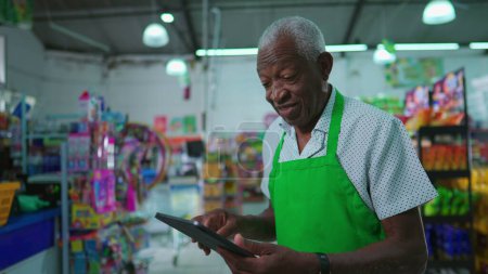 Téléchargez les photos : Cadres supérieurs afro-américains du supermarché utilisant un appareil tablette debout à l'intérieur de l'épicerie, profession d'une personne âgée noire sur le lieu de travail, vérification de l'inventaire - en image libre de droit