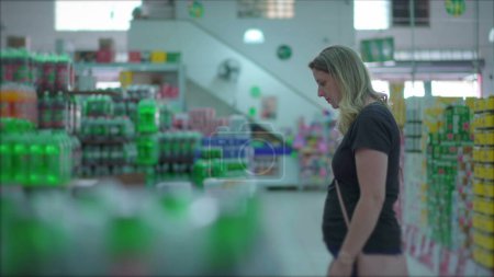 Téléchargez les photos : Acheteuse femelle réfléchissant à l'achat de boissons gazeuses allée du supermarché - en image libre de droit