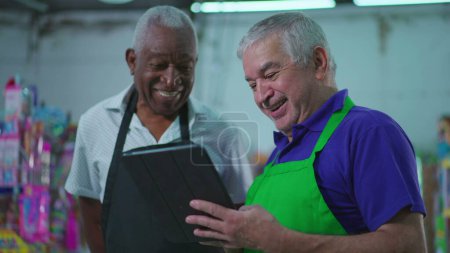 Photo for Diverse Senior Employees at Supermarket holding tablet device pointing at Grocery Store inventory, Teamwork Scene of Older Manager Guiding Employee - Royalty Free Image