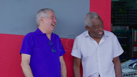 Foto de Dos felices y diversos amigos mayores abrazándose y celebrando con los cinco de pie afuera en la acera. Alegre compañía afroamericana y caucásica auténtica interacción - Imagen libre de derechos