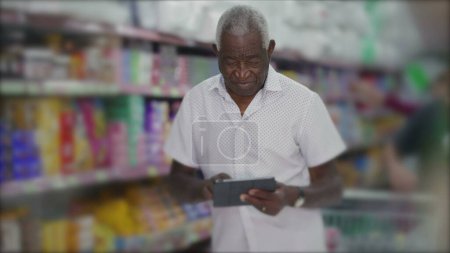 Téléchargez les photos : Un gestionnaire noir de l'inventaire de navigation de l'épicerie avec tablette debout dans l'allée. Propriétaire de petite entreprise inspectant les produits avec la technologie moderne - en image libre de droit