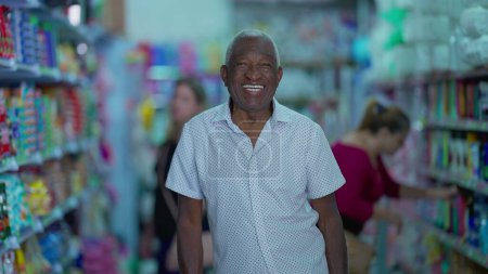 Téléchargez les photos : Un gestionnaire brésilien senior noir de l'épicerie tenant tablette posant pour appareil photo à l'intérieur de la petite entreprise. Une personne afro-américaine plus âgée utilisant la technologie moderne - en image libre de droit