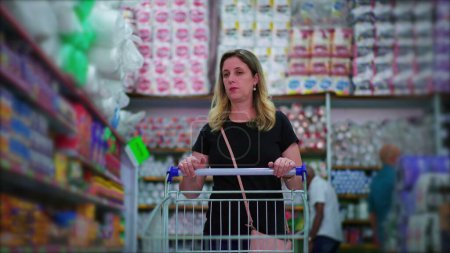 Téléchargez les photos : Acheteuse marchant à l'épicerie allée poussant panier d'achat produits de navigation sur étagère, représentant les habitudes de vie des consommateurs - en image libre de droit