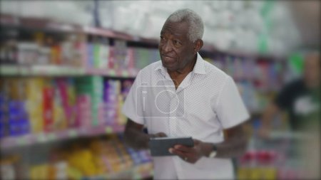 Téléchargez les photos : Un gestionnaire noir de l'inventaire de navigation de l'épicerie avec tablette debout dans l'allée. Propriétaire de petite entreprise inspectant les produits avec la technologie moderne - en image libre de droit