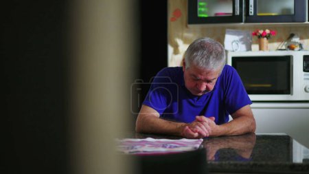 Photo for Preoccupied senior man at kitchen table ruminating problems, candid domestic scene of elderly person going through difficulties and loneliness - Royalty Free Image