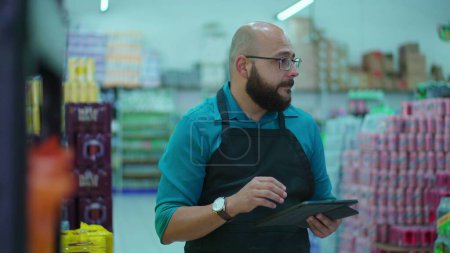 Foto de Empleado alegre del retrato de la tienda de comestibles sonriendo a la cámara de pie en el pasillo del supermercado usando delantal, el concepto de ocupación de trabajo del personal masculino - Imagen libre de derechos