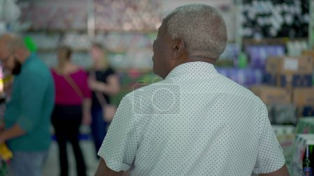 Téléchargez les photos : Homme noir âgé faisant des achats dans un supermarché, vue arrière du chariot pousseur Shopper et regardant des produits - en image libre de droit