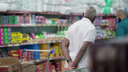 Photo for Back of a senior customer browsing at products at grocery store, looking at items to buy on shelf. Elderly shopper in candid scene, consumer lifestyle - Royalty Free Image