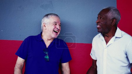 Photo for Seniors Leaning on Wall, Interacting with Laughter on Street, African American and Caucasian Older Men talking in candid conversation in urban setting - Royalty Free Image