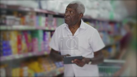 Photo for One black manager of grocery store browsing inventory with tablet device standing in aisle. Small business owner inspecting products with modern technology - Royalty Free Image