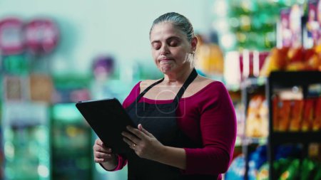 Photo for Stressed female entrepreneur owner of small business struggling with hard times holding tablet and staring at the bottom line of the grocery store - Royalty Free Image