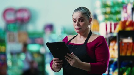 Photo for Stressed female entrepreneur owner of small business struggling with hard times holding tablet and staring at the bottom line of the grocery store - Royalty Free Image