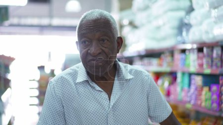 Photo for One happy African American senior man pushing shopping cart at grocery store. Portrait of an elderly black consumer at local business store aisle with products - Royalty Free Image