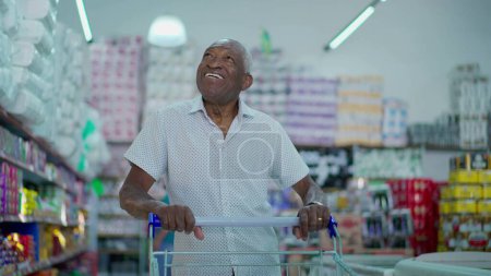 Photo for One joyful black Brazilian man pushing shopping cart at grocery store. African American consumer browsing for products to buy, looking at shelves - Royalty Free Image