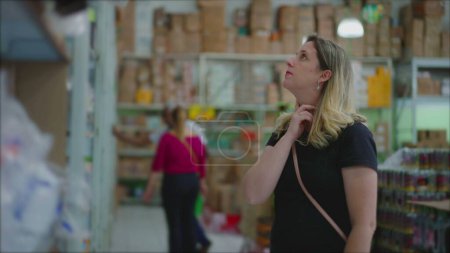 Foto de Consumo femenino que busca productos en el estante en la tienda de comestibles, considerando mercancía para la venta, decisión de ponderación, hábitos de estilo de vida de consumismo - Imagen libre de derechos