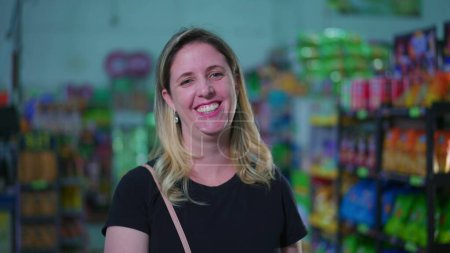 Téléchargez les photos : Joyeuse consommatrice debout à l'intérieur d'un supermarché souriant à la caméra et tenant le panier, portrait en gros plan d'une femme heureuse représentant l'habitude du mode de vie consumériste - en image libre de droit