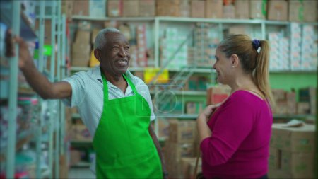 Photo for Happy African American employee and female customer laughing and smiling together standing by supermarket aisle. joyful authentic everyday people - Royalty Free Image