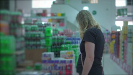 Téléchargez les photos : Femme inspectant des articles dans Supermarket _ s Soda Drink Section - en image libre de droit