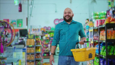 Foto de Hombre brasileño feliz parado en la tienda de comestibles sosteniendo la cesta en la mano sonriendo a la cámara, hábitos de consumo del supermercado sudamericano - Imagen libre de derechos