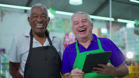 Foto de Candid Authentic Joy Between Older Supermarket Colleagues doing high-five, Smiling Diverse Senior Men with Tablet Device, workers celebrating success - Imagen libre de derechos