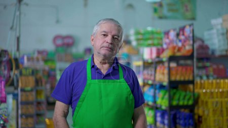 Photo for Concerned senior manager of grocery store wearing apron standing inside small business with worried expression. Gray haired elderly employee of supermarket - Royalty Free Image