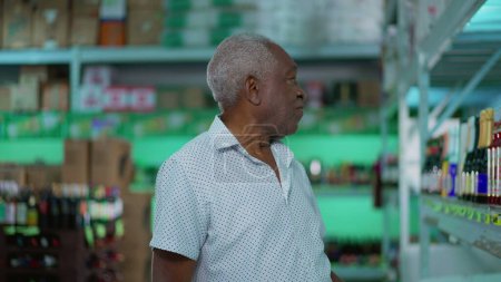 Téléchargez les photos : Homme afro-américain âgé sélectionnant des boissons alcoolisées au supermarché, un acheteur noir senior dans l'allée des boissons - en image libre de droit