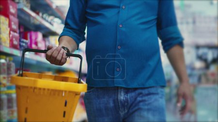 Photo for Detailed close-up of a shopper_s hand holding a supermarket basket, browsing products while walking down a grocery store aisle - Royalty Free Image