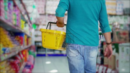 Photo for Back of shopper walking in supermarket aisle holding basket in hand, close-up detail of consumer at grocery store - Royalty Free Image