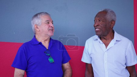 Foto de Dos ancianos brasileños diversos de pie en la calle conversando e intercambiando historias mientras ríen y sonríen, franca interacción auténtica de ancianos en América del Sur - Imagen libre de derechos