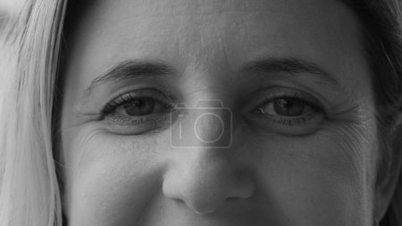 Téléchargez les photos : Macro gros plan serré d'une femme dans la quarantaine souriant à l'appareil photo en photographie noir et blanc. Personne monochromatique expression heureuse - en image libre de droit